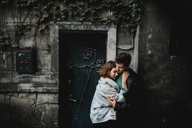 Jovem casal abraça suavemente perto da parede de um edifício antigo