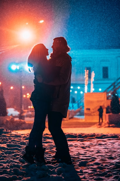 Jovem casal adulto nos braços um do outro na rua coberta de neve