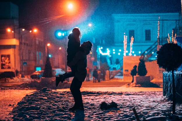 Jovem casal adulto nos braços um do outro na rua coberta de neve