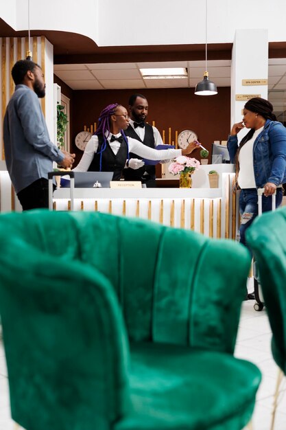 Jovem casal afro-americano chegando ao hotel, parado na recepção com bagagem conversando com a recepcionista durante o check-in. Agente da recepção obtendo informações sobre os hóspedes durante o check-in