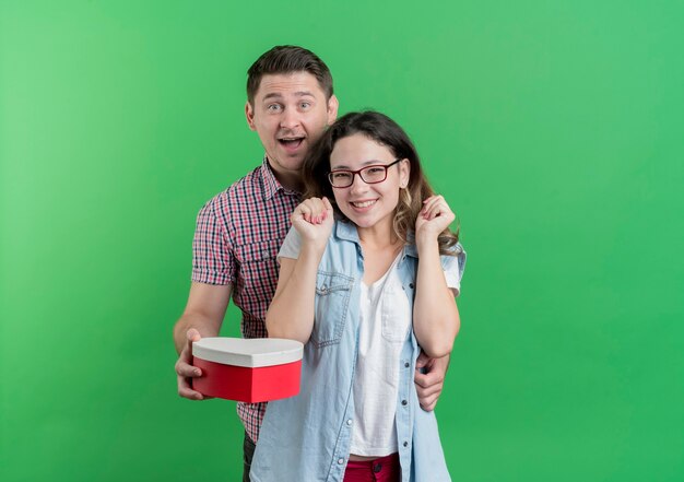 Foto grátis jovem casal alegre feliz entregando uma caixa de presente para sua namorada surpresa e sorridente no verde