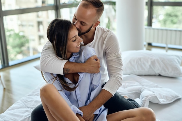 Jovem casal apaixonado passando a manhã juntos no quarto Homem está abraçando e beijando sua namorada