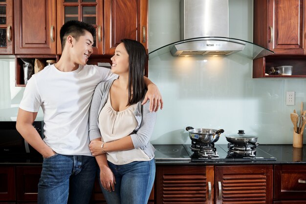 Jovem casal asiático feliz dançando na cozinha em casa, abraçando e olhando um ao outro