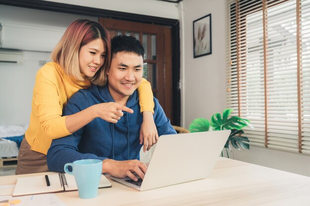 Jovem casal asiático gerenciando finanças, revendo suas contas bancárias usando o computador portátil