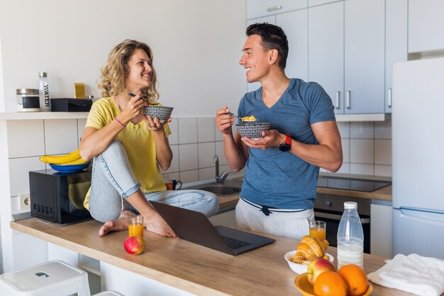 Jovem casal atraente de um homem e uma mulher tomando café da manhã juntos pela manhã na cozinha