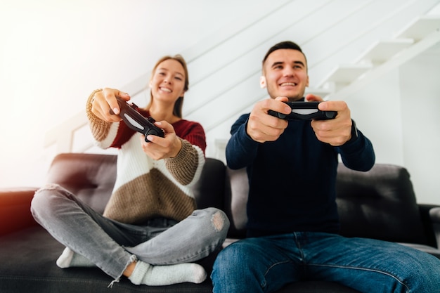 Jovem casal atraente engraçado jogar jogos de computador com joysticks, sentado no sofá