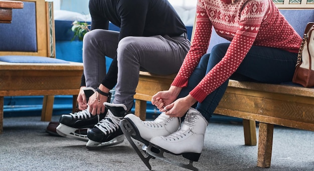 Jovem casal atraente sentado em um banco e amarrando cadarços de patins de hóquei no gelo no vestiário