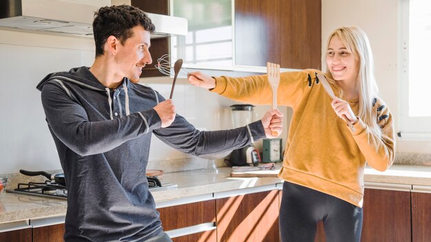 Jovem casal brigando com espátula de madeira; colher e bata na cozinha