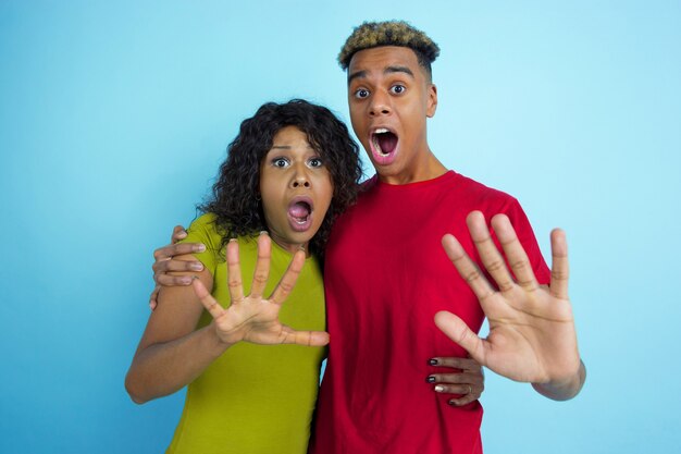 Jovem casal chocado com roupas casuais posando na parede azul