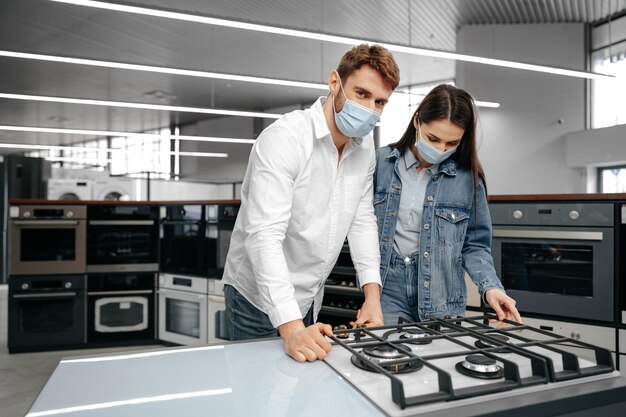 Jovem casal com máscaras médicas olhando para eletrodomésticos em um shopping