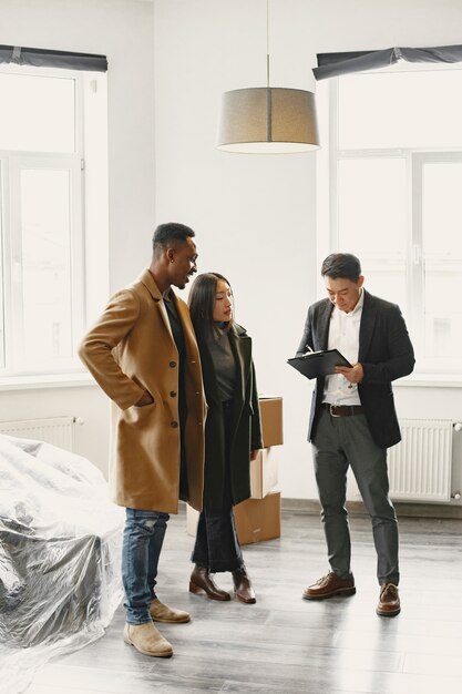 Jovem Casal Comprando Uma Casa Nova. Mulher asiática e homem africano. Assinatura de documentos na nova casa.