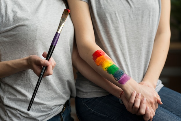 Jovem casal de lésbicas, segurando a mão do outro com bandeira de arco-íris pintada por lado