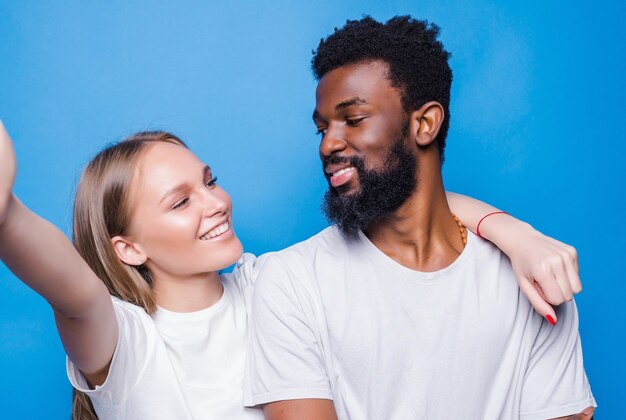 Jovem casal de raça mista tirando uma selfie isolada na parede azul