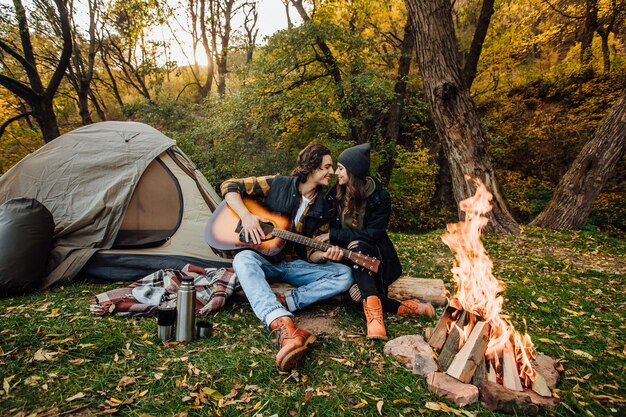 Jovem casal de turistas relaxando perto do fogo na natureza