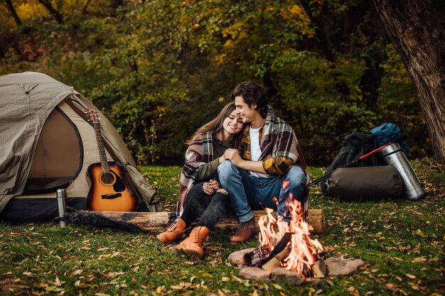 Jovem casal de turistas relaxando perto do fogo na natureza