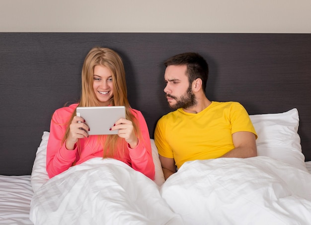 Foto grátis jovem casal doce na cama assistindo algo no tablet gadget. conceito sobre tecnologia e pessoas