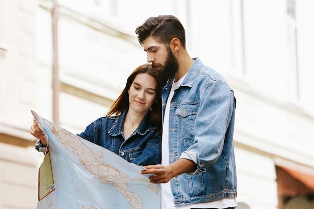 Jovem casal em roupas de jeans fica com mapa turista em algum lugar da cidade velha