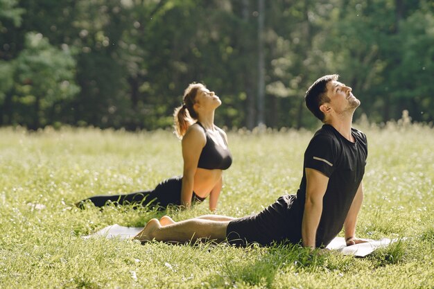 Jovem casal esportivo fazendo ioga fitness. Pessoas em um parque de verão.