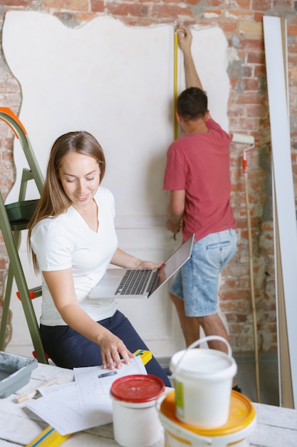 Foto grátis jovem casal fazendo conserto de apartamento juntos. homem casado e mulher fazendo reforma ou reforma em casa. conceito de relações, família, amor. medir a parede antes de pintar, fazer design.