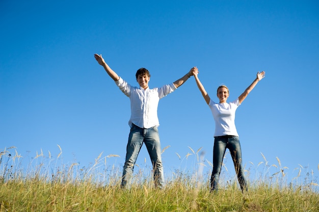 Jovem casal feliz dançando juntos em um prado de verão com as mãos ao alto