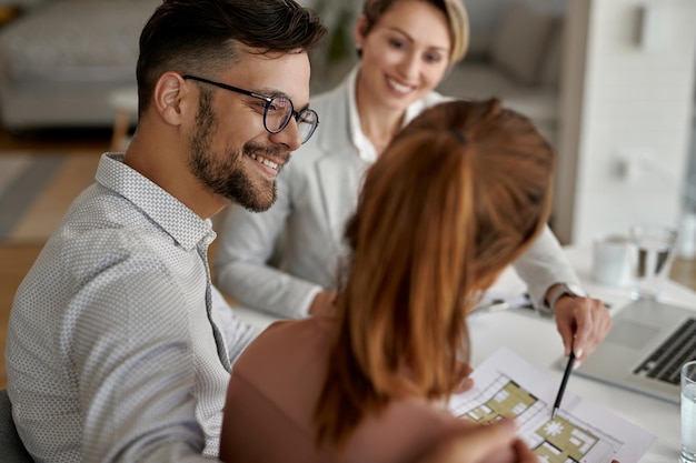 Jovem casal feliz e seu agente imobiliário tendo uma reunião no escritório o foco está no homem