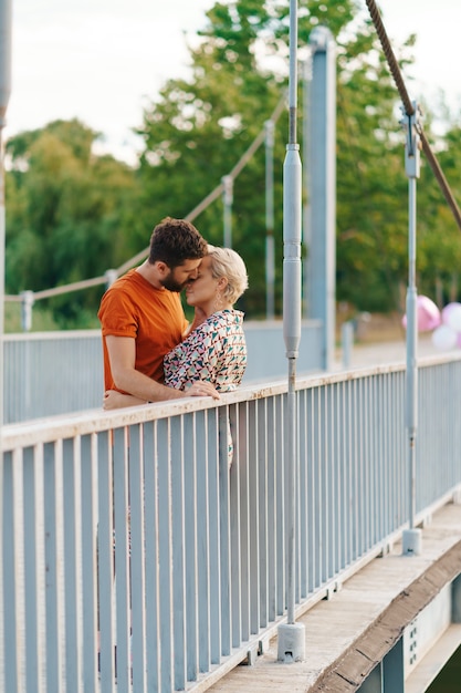 Jovem casal feliz e sorridente se abraçando e beijando na ponte