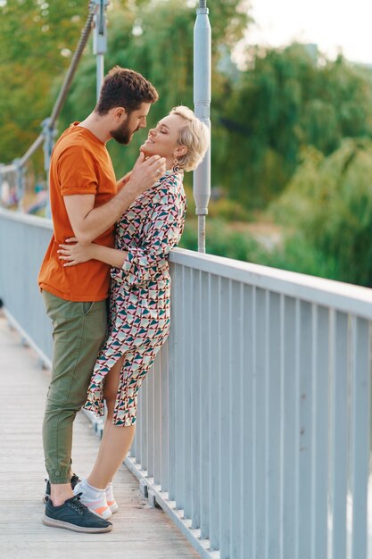 Jovem casal feliz e sorridente se abraçando e beijando na ponte