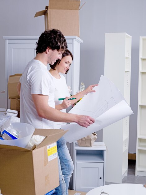 Jovem casal feliz em seu novo apartamento com um plano nas mãos