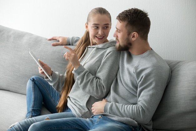 Jovem casal feliz falando sentado no sofá usando tablet digital