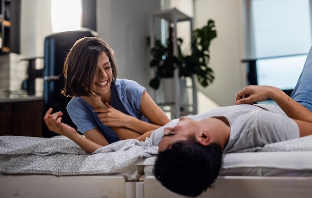 Jovem casal feliz se divertindo juntos enquanto estava deitado na cama e se comunicando