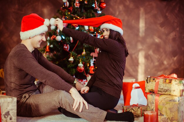 Jovem casal feliz vestindo chapéus de santa no estúdio