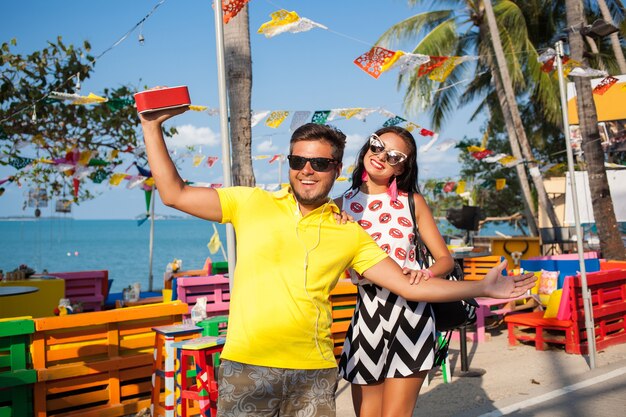 Jovem casal hippie elegante nas férias de verão na Tailândia, glamour, roupas de tendências da moda, óculos de sol, romance tropical, sorrindo, feliz, ouvindo música, clima de festa, café na praia