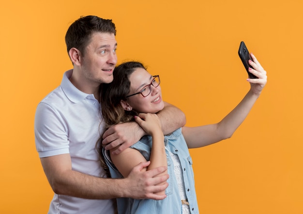 Foto grátis jovem casal homem e mulher com roupas casuais juntos fazendo selfie feliz no amor se divertindo com laranja
