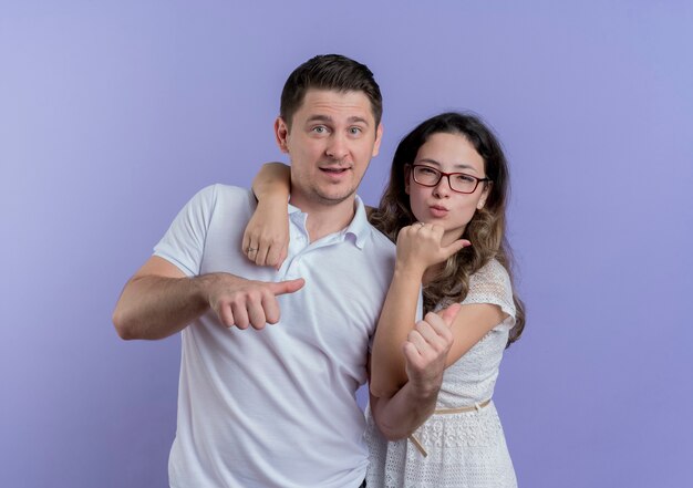 Jovem casal, homem e mulher, olhando para a câmera sorrindo alegremente em pé sobre a parede azul