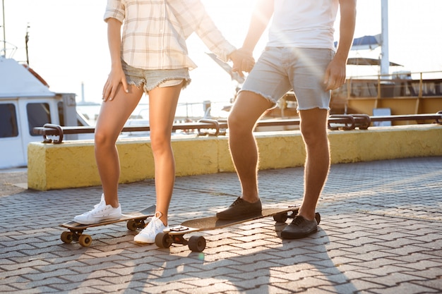 Jovem casal lindo andando na beira-mar, andar de skate. Feche de pernas.