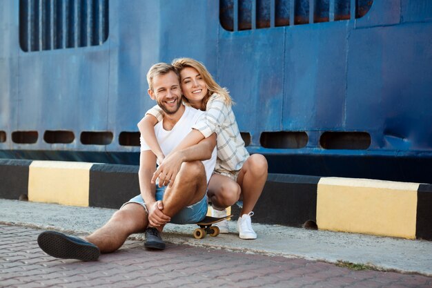 Jovem casal lindo andando pela cidade, sorrindo, sentado de patins.