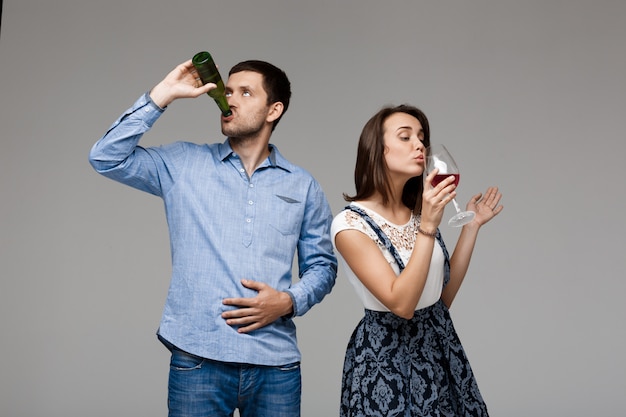 Jovem casal lindo bebendo vinho e cerveja sobre parede cinza