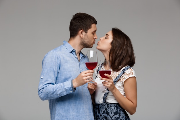 Jovem casal lindo bebendo vinho sobre parede cinza