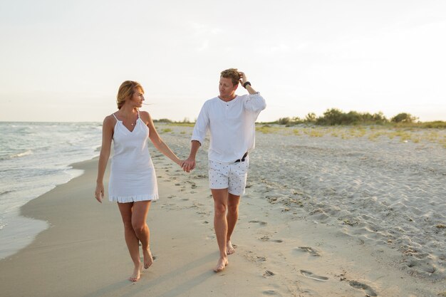 Jovem casal lindo caminha à beira-mar ao pôr do sol.