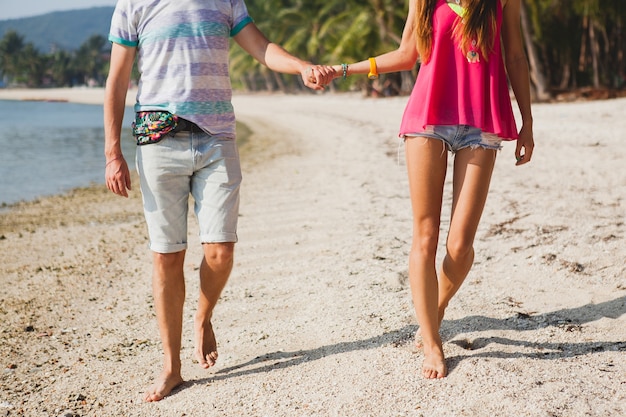 Jovem casal lindo caminhando em uma praia tropical, Tailândia, de mãos dadas, vista de trás, roupa hipster, estilo casual, lua de mel, férias, verão, clima romântico, close-up de pernas, detalhes