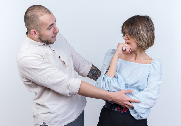 Jovem casal lindo com roupas casuais, homem e mulher brigando, olhando um para o outro em pé sobre uma parede branca