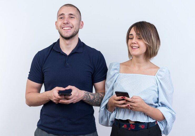 Foto grátis jovem casal lindo com roupas casuais, homem e mulher feliz e positiva segurando smartphones, olhando de lado com um sorriso no rosto em pé
