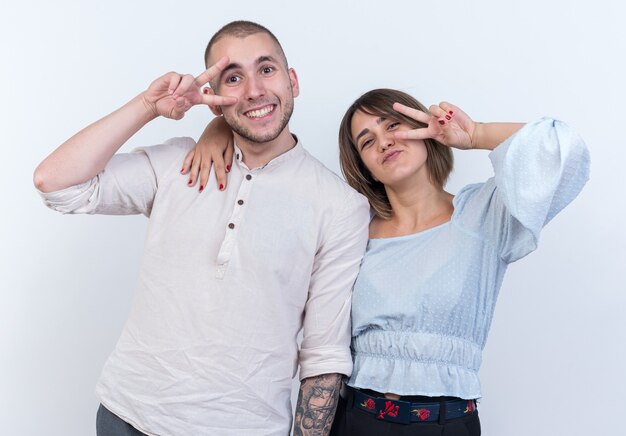 Foto grátis jovem casal lindo com roupas casuais, homem e mulher felizes e positivos, mostrando o sinal-v em pé sobre uma parede branca
