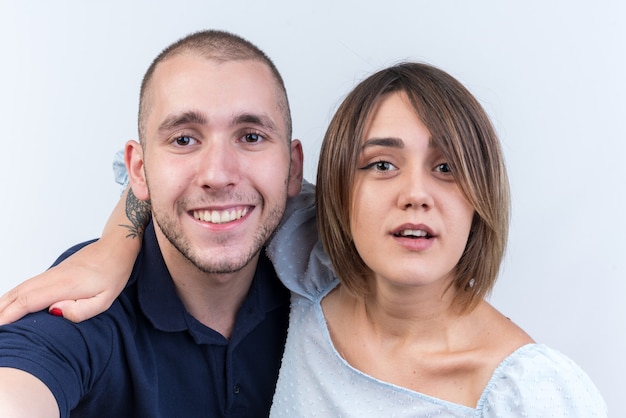 Jovem casal lindo com roupas casuais, homem e mulher, felizes e positivos, sorrindo alegremente em pé sobre uma parede branca