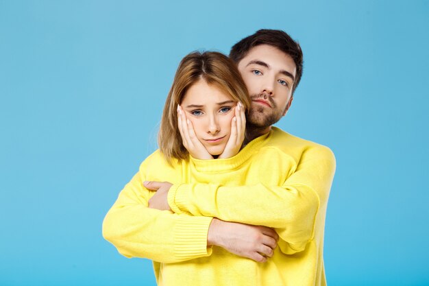 Jovem casal lindo em uma camisola amarela abraçando sorrindo sobre parede azul