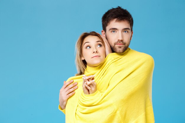 Jovem casal lindo em uma camisola amarela abraçando sorrindo sobre parede azul