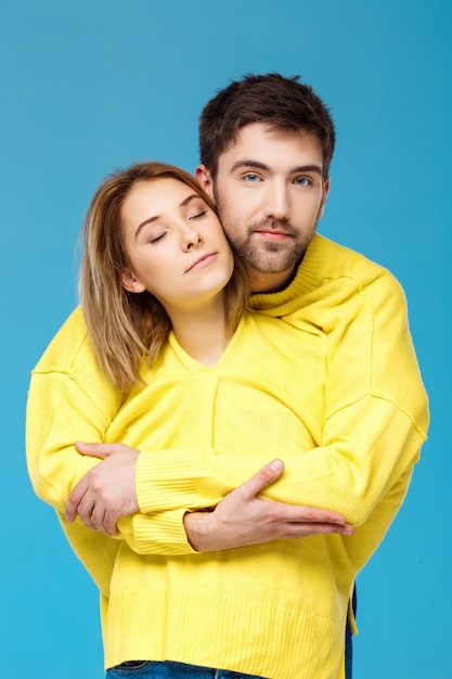 Jovem casal lindo em uma camisola amarela abraçando sorrindo sobre parede azul