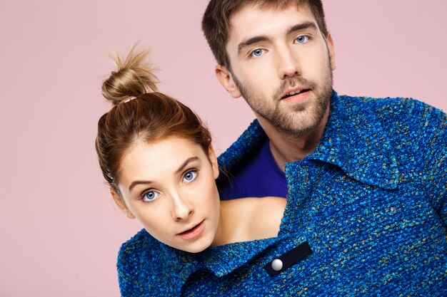 Jovem casal lindo em uma camisola de malha azul posando sorrindo se divertindo sobre parede rosa clara