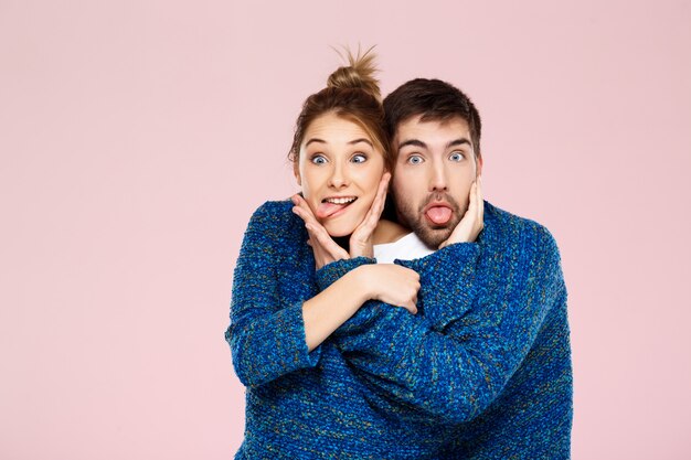 Jovem casal lindo em uma camisola de malha azul posando sorrindo se divertindo sobre parede rosa clara