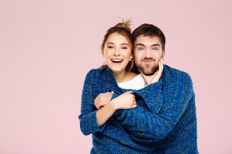 Foto grátis jovem casal lindo em uma camisola de malha azul posando sorrindo se divertindo sobre parede rosa clara